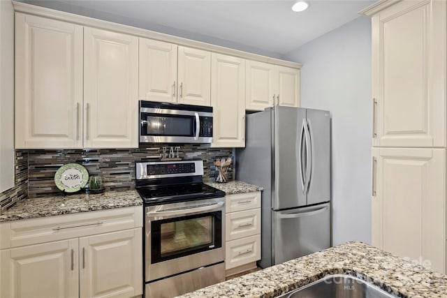 kitchen featuring tasteful backsplash, cream cabinets, light stone counters, and appliances with stainless steel finishes