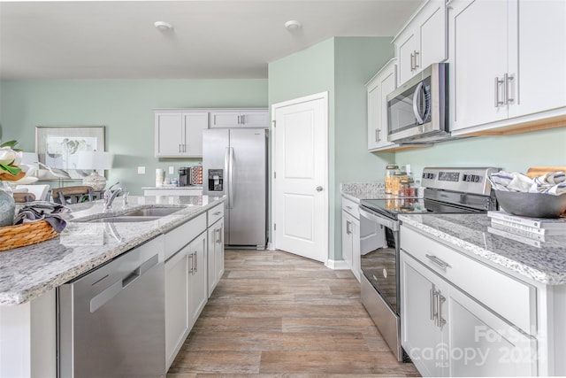 kitchen with appliances with stainless steel finishes, sink, white cabinetry, light hardwood / wood-style flooring, and a center island with sink