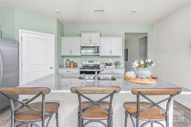 kitchen with a breakfast bar, light wood-type flooring, white cabinetry, appliances with stainless steel finishes, and light stone counters