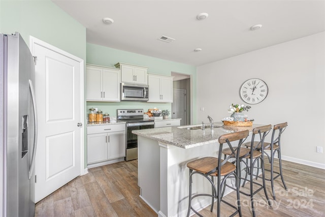 kitchen featuring a kitchen island with sink, sink, hardwood / wood-style floors, white cabinets, and appliances with stainless steel finishes