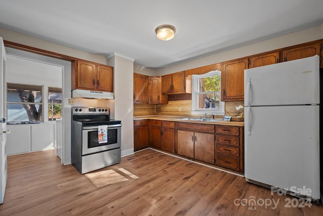 kitchen featuring stainless steel electric stove, decorative backsplash, white fridge, and light wood-type flooring