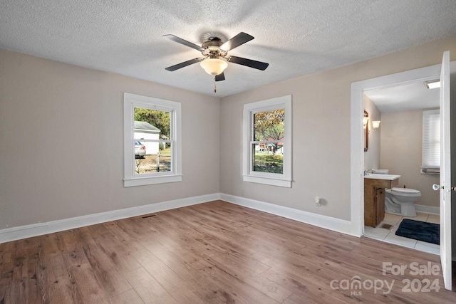 unfurnished bedroom featuring ceiling fan, light hardwood / wood-style floors, ensuite bathroom, and a textured ceiling