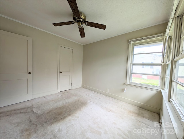 unfurnished bedroom with light colored carpet, a textured ceiling, ceiling fan, crown molding, and a closet