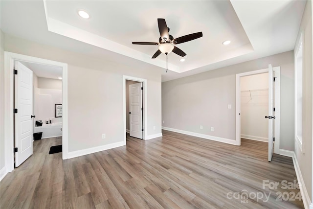 unfurnished bedroom featuring a raised ceiling, ceiling fan, a closet, light hardwood / wood-style floors, and a walk in closet