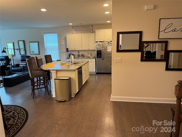 kitchen with white cabinets, a center island with sink, light stone counters, and appliances with stainless steel finishes