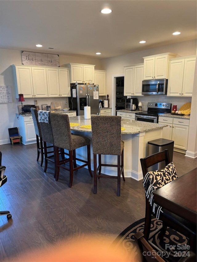 kitchen with light stone counters, a center island with sink, appliances with stainless steel finishes, white cabinets, and a breakfast bar area