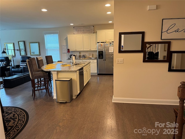 kitchen with stainless steel appliances, a sink, dark wood finished floors, white cabinets, and light stone countertops