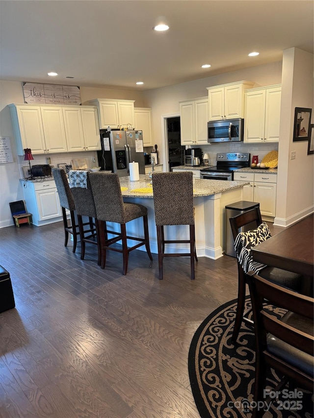 kitchen with stainless steel appliances, white cabinetry, dark wood-style flooring, a breakfast bar, and recessed lighting