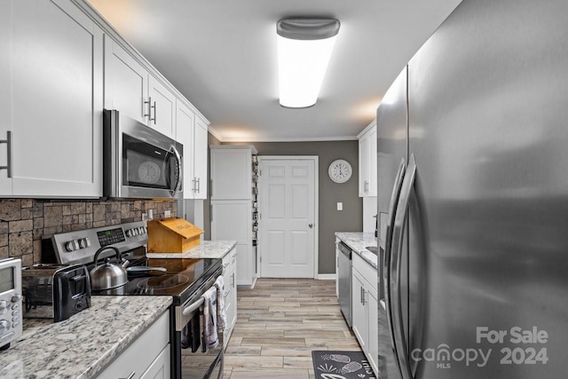 kitchen featuring light stone counters, ornamental molding, appliances with stainless steel finishes, white cabinets, and light hardwood / wood-style flooring