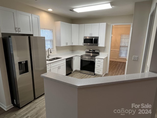 kitchen featuring appliances with stainless steel finishes, sink, light hardwood / wood-style floors, white cabinets, and light stone counters