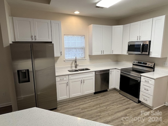 kitchen featuring stainless steel appliances, sink, light wood-type flooring, and white cabinets