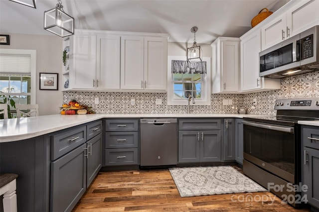 kitchen featuring white cabinets, hanging light fixtures, appliances with stainless steel finishes, light hardwood / wood-style flooring, and gray cabinets