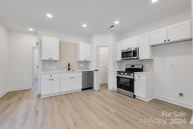 kitchen with stainless steel appliances, a sink, backsplash, white cabinetry, and recessed lighting