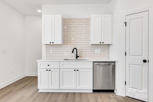 kitchen with stainless steel dishwasher, a sink, white cabinetry, backsplash, and light countertops