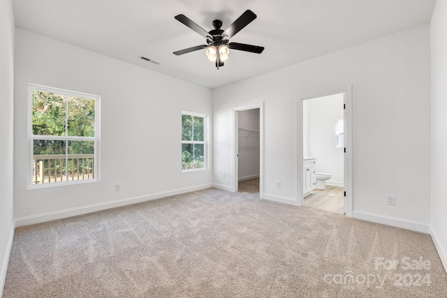 unfurnished bedroom featuring a closet, ensuite bath, a spacious closet, light colored carpet, and ceiling fan