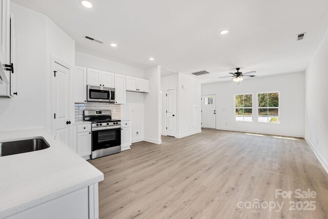 606 Meadow St, Spencer, NC 28159 - kitchen with appliances with stainless steel finishes, ceiling fan, backsplash, white cabinetry, and light wood-style flooring