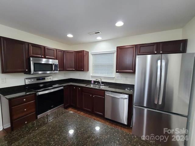 kitchen featuring dark hardwood / wood-style flooring, sink, stainless steel appliances, and dark stone counters