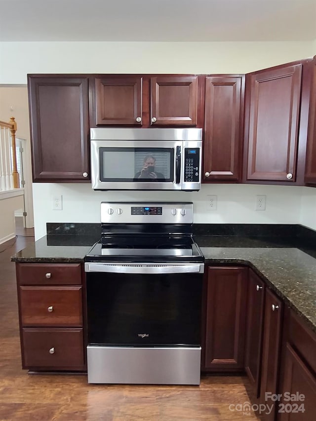 kitchen with appliances with stainless steel finishes, hardwood / wood-style floors, and dark stone counters