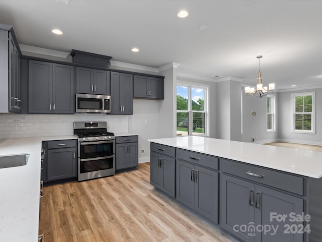 kitchen with appliances with stainless steel finishes, pendant lighting, light hardwood / wood-style floors, crown molding, and gray cabinetry