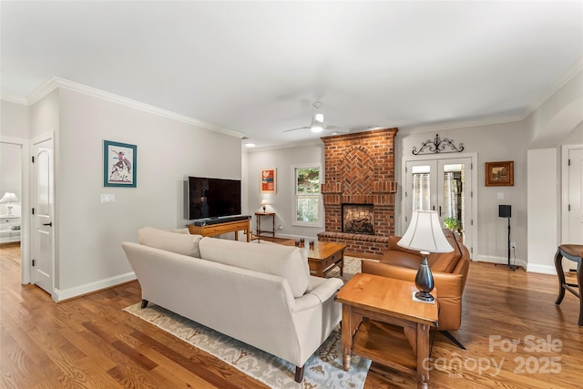 living room with french doors, a fireplace, light wood-type flooring, ceiling fan, and crown molding