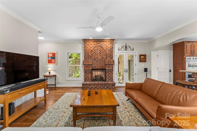 living room featuring hardwood / wood-style flooring, ceiling fan, ornamental molding, and a fireplace