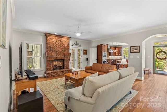 living room with a fireplace, light hardwood / wood-style flooring, ceiling fan, and ornamental molding