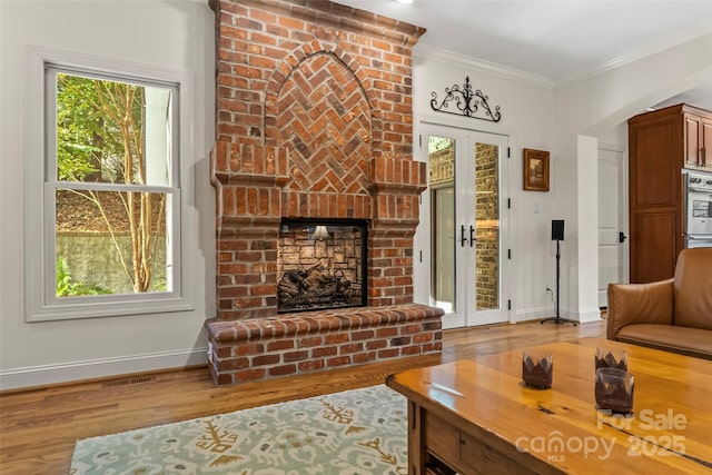 living room featuring light wood-type flooring, crown molding, french doors, and a fireplace