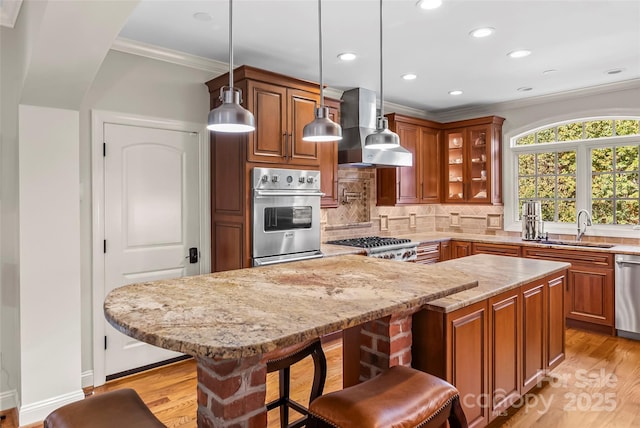 kitchen featuring wall chimney exhaust hood, light stone countertops, a kitchen bar, ornamental molding, and stainless steel appliances