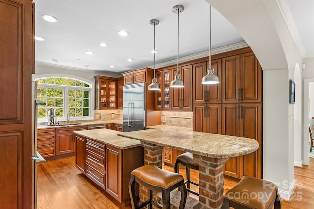 kitchen featuring tasteful backsplash, a kitchen breakfast bar, built in refrigerator, sink, and pendant lighting