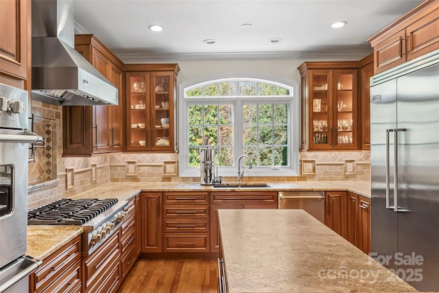 kitchen featuring wall chimney range hood, stainless steel appliances, decorative backsplash, sink, and ornamental molding