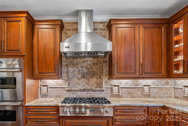 kitchen featuring light stone countertops, wall chimney exhaust hood, stainless steel appliances, decorative backsplash, and crown molding