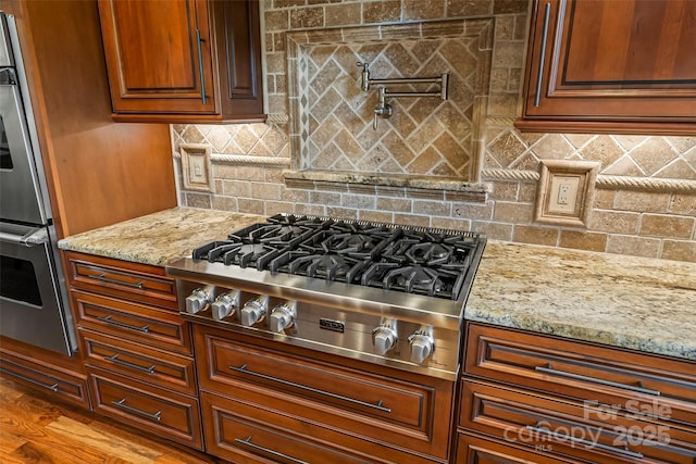 kitchen featuring light stone counters, hardwood / wood-style flooring, decorative backsplash, and stainless steel appliances