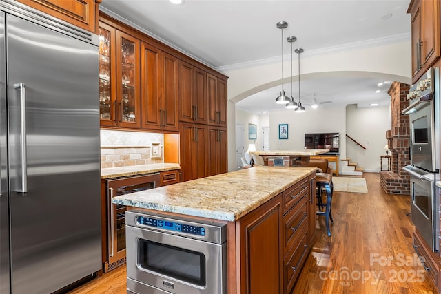 kitchen with built in appliances, a center island, hanging light fixtures, backsplash, and beverage cooler