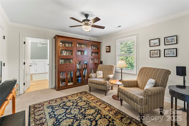 sitting room with ceiling fan, light colored carpet, and crown molding