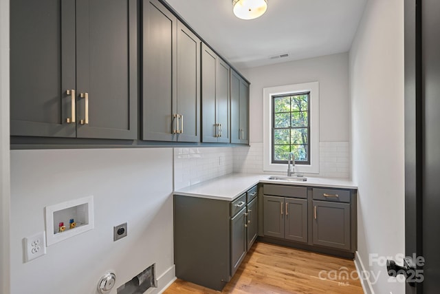 laundry room featuring electric dryer hookup, light wood-type flooring, washer hookup, cabinets, and sink