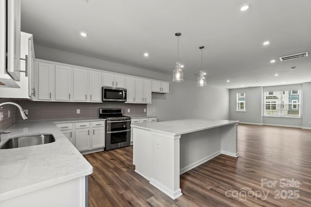 kitchen featuring white cabinets, stainless steel appliances, a center island, sink, and backsplash