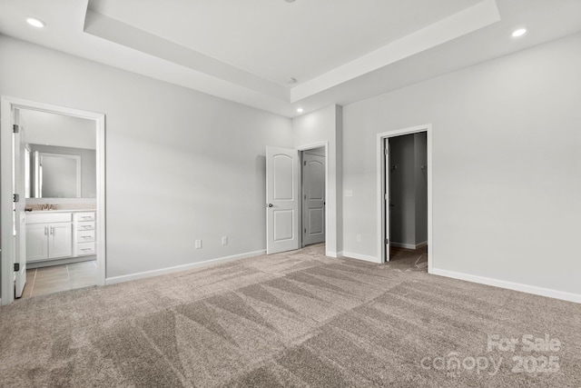 unfurnished bedroom with light colored carpet, a walk in closet, ensuite bath, and a tray ceiling