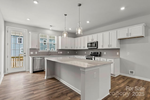 kitchen with stainless steel appliances, white cabinetry, a kitchen island, and light stone counters