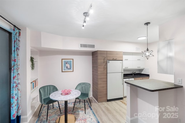 kitchen featuring white cabinetry, hanging light fixtures, kitchen peninsula, light hardwood / wood-style floors, and white appliances