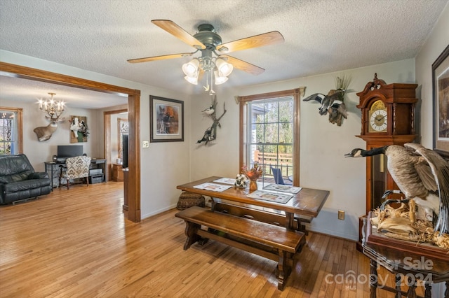 dining area with ceiling fan with notable chandelier, a textured ceiling, and light wood-type flooring