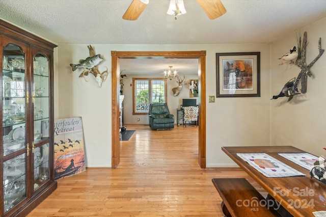 corridor featuring light hardwood / wood-style flooring, a textured ceiling, and an inviting chandelier