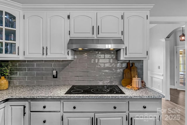 kitchen with black electric stovetop, extractor fan, light stone countertops, and white cabinets