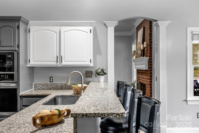 kitchen featuring white cabinetry, oven, sink, and light stone counters