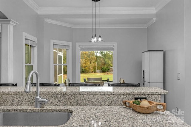 kitchen featuring light stone counters, decorative light fixtures, sink, and crown molding