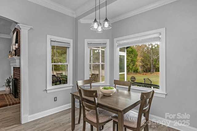 dining space featuring a brick fireplace, hardwood / wood-style flooring, ornamental molding, and a healthy amount of sunlight