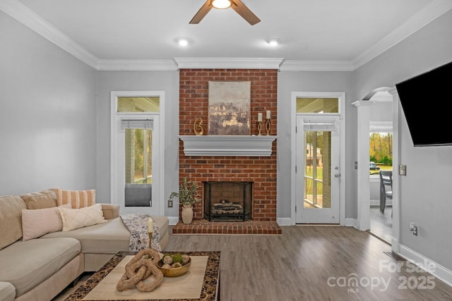 living room with hardwood / wood-style flooring, ceiling fan, ornamental molding, and a brick fireplace