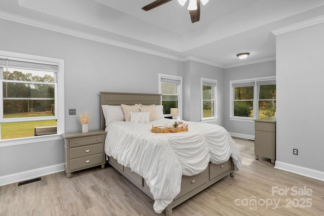 bedroom featuring a tray ceiling, crown molding, ceiling fan, and light wood-type flooring