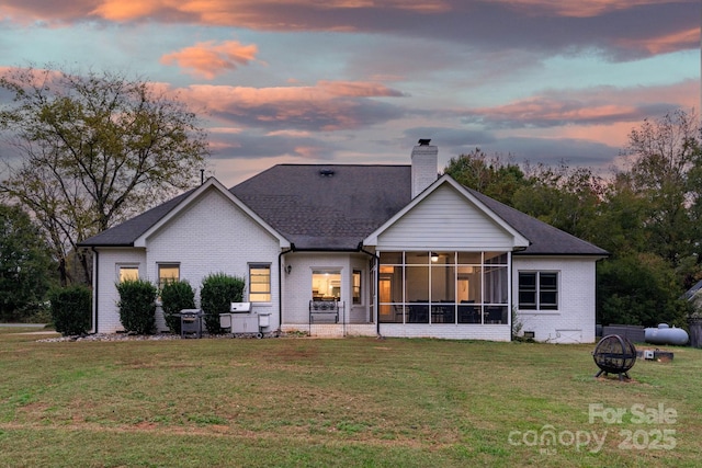 back house at dusk with a fire pit, a lawn, and a sunroom