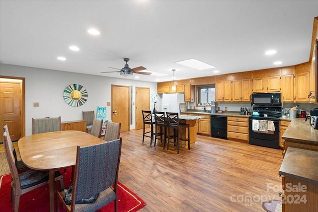 dining area with ceiling fan, sink, light wood-type flooring, and a skylight