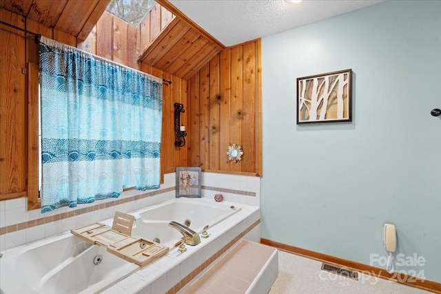 bathroom featuring tiled bath, a textured ceiling, wooden walls, and lofted ceiling with skylight